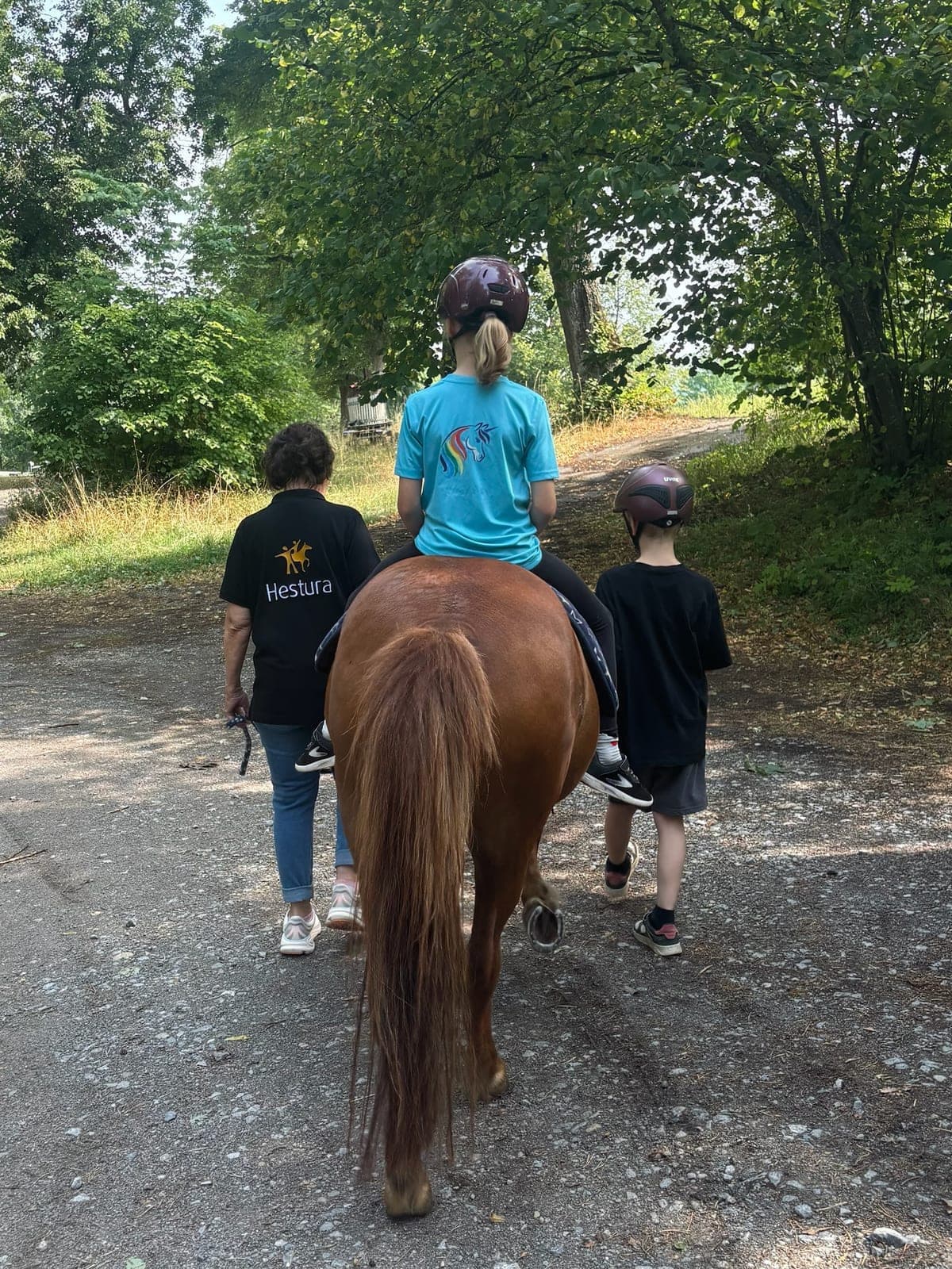 Kind reitet auf einem Pony über einen Feldweg, zwei Begleitpersonen gehen nebenher