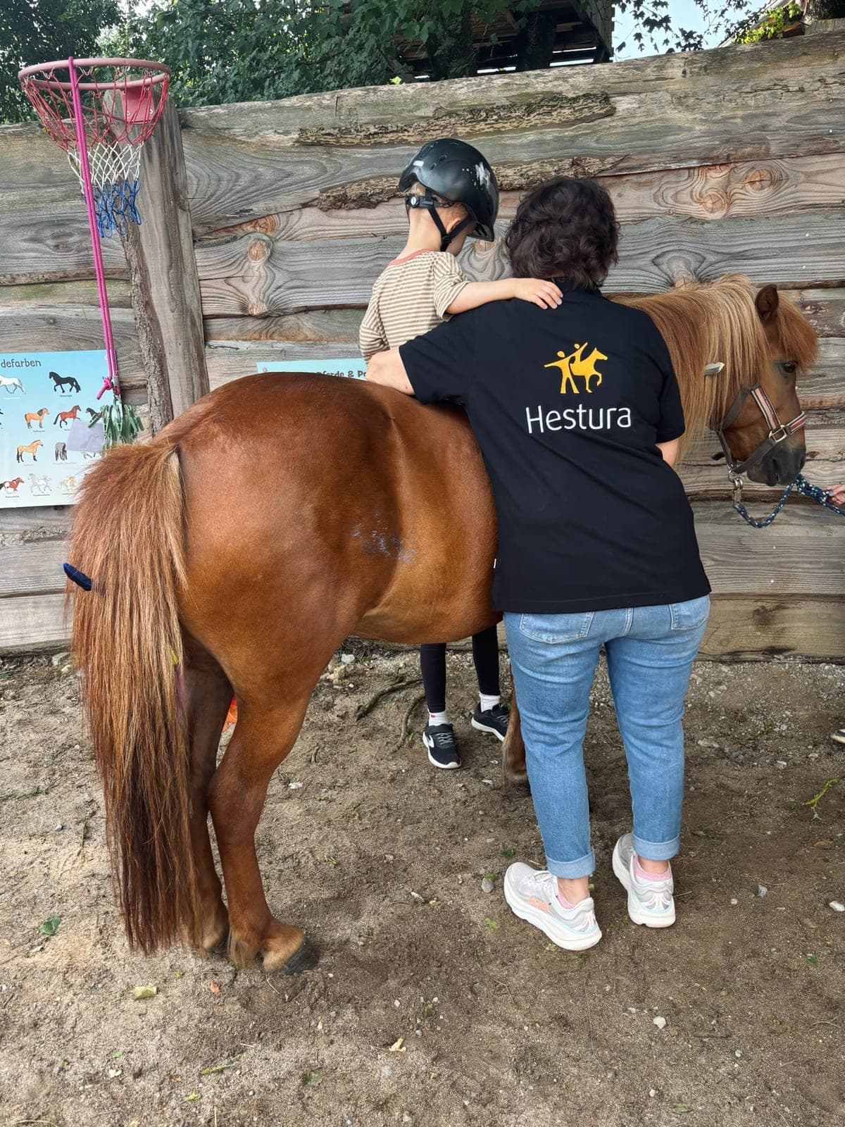 Kind sitzt auf einem Pony, eine Begleiterin steht führend daneben