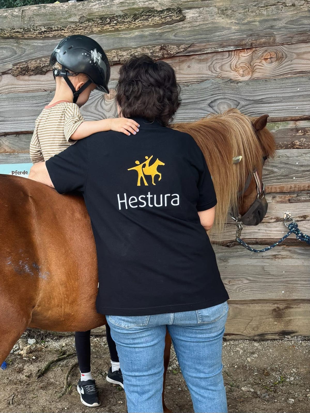 Kind auf einem Pony stützt sich beim Reiten auf die Schulter der Begleiterin